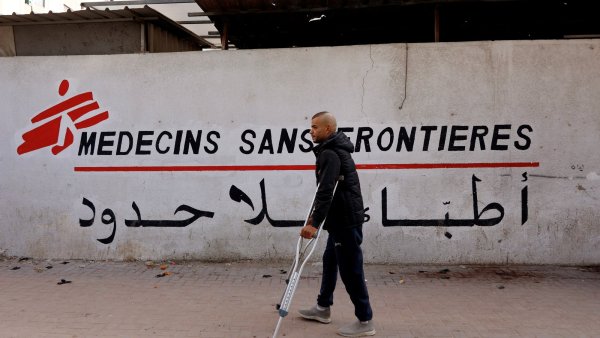 Un homme avec des béquilles marche devant un mur portant le logo de Médecins Sans Frontières.