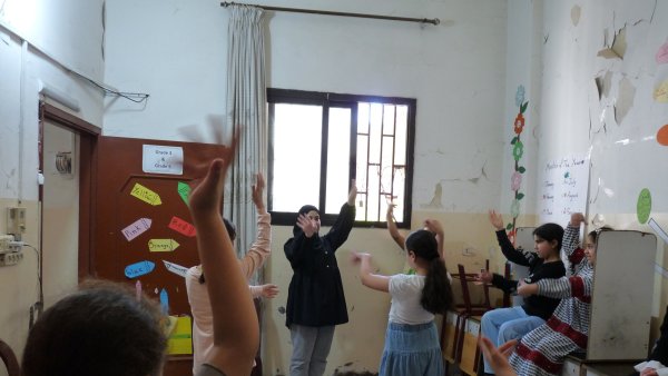 Un groupe d'enfants danse en cercle dans une salle avec des murs abîmés.
