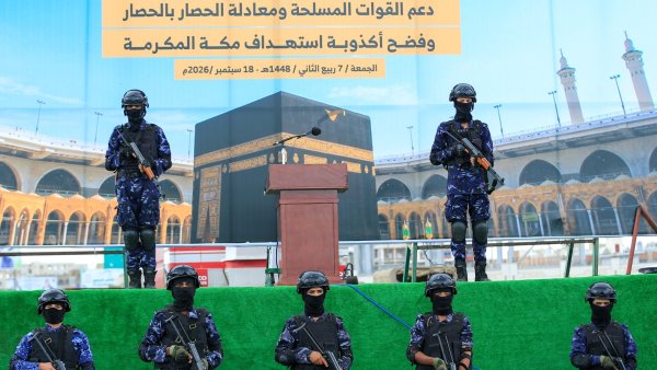 Six soldats en uniforme noir se tiennent devant un décor de la Mecque, armés.