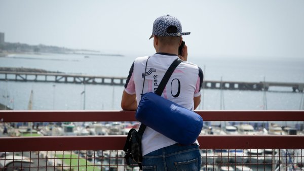 Un homme regarde la mer depuis un pont, avec un port et des bateaux en arrière-plan.