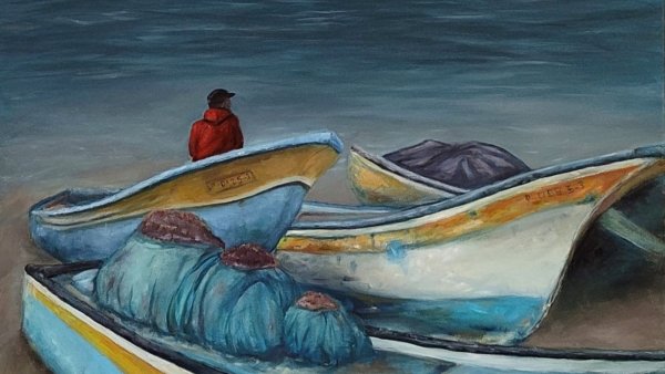 Un homme assis près de bateaux colorés sur une plage, face à la mer calme.