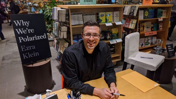 Un homme souriant est assis à une table, entouré de livres et de matériel de dédicace.