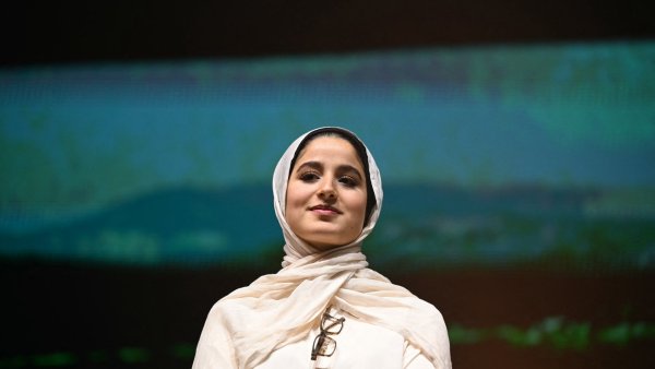 Femme en hijab, regard confiant, léger sourire, fond flou évoquant un paysage.