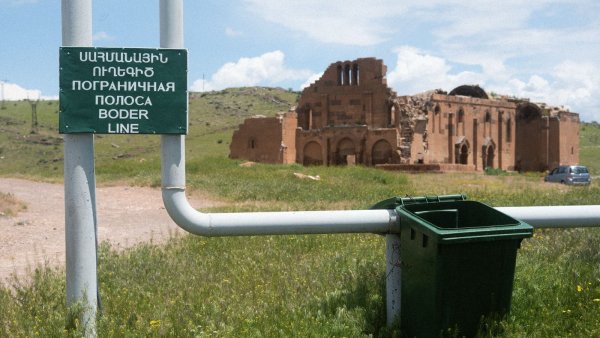 Ruines d'un bâtiment ancien avec un panneau et une poubelle au premier plan.