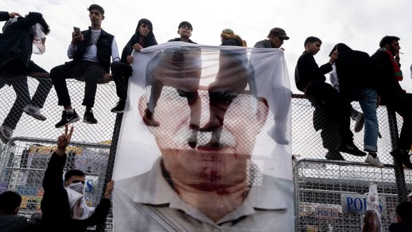 Des personnes assises sur une barrière, tenant une grande affiche d'un homme.