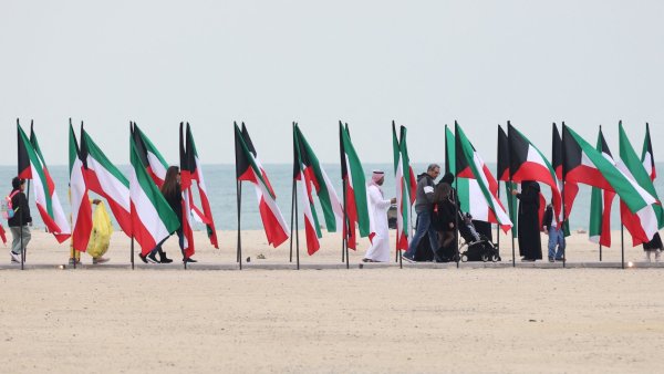 Des gens marchent devant des drapeaux du Koweït sur une plage.