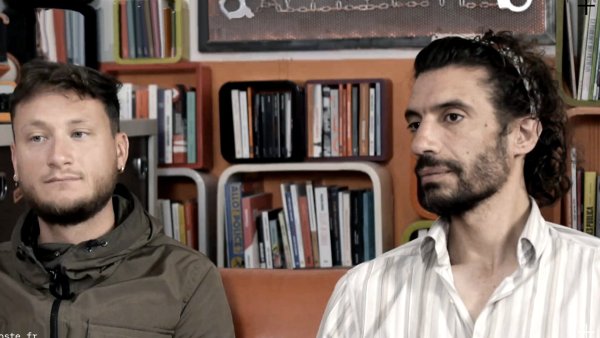Deux hommes assis, l'un en veste, l'autre en chemise, devant une étagère de livres.