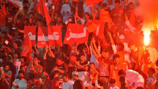 Supporters en fête, agitant des drapeaux rouges et des affichettes dans une ambiance dynamique.