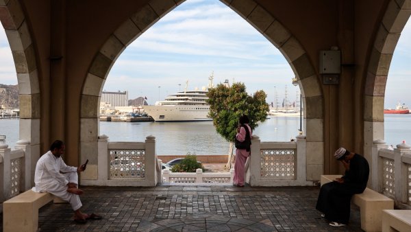 Vue d'un port avec un yacht, entourée d'une architecture arabe, des personnes assises.