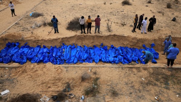 Des corps enveloppés de bleu sont placés dans une fosse, entourés de personnes en deuil.