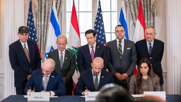 Des personnes signent un accord, entourées de drapeaux et en présence d'observateurs.