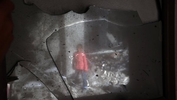 Un enfant en manteau rouge se reflète dans un miroir brisé.