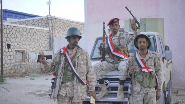 Trois soldats armés posent sur un véhicule, en uniforme camouflage et écharpes tricolores.