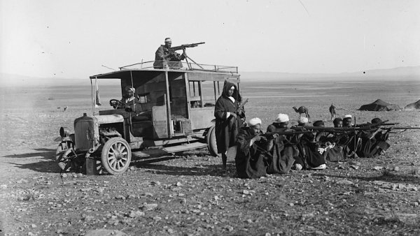 Une vieille voiture militaire avec des soldats armés et des hommes assis au sol.