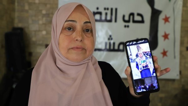 Femme en hijab montrant une photo sur son téléphone, avec un arrière-plan de banderole.